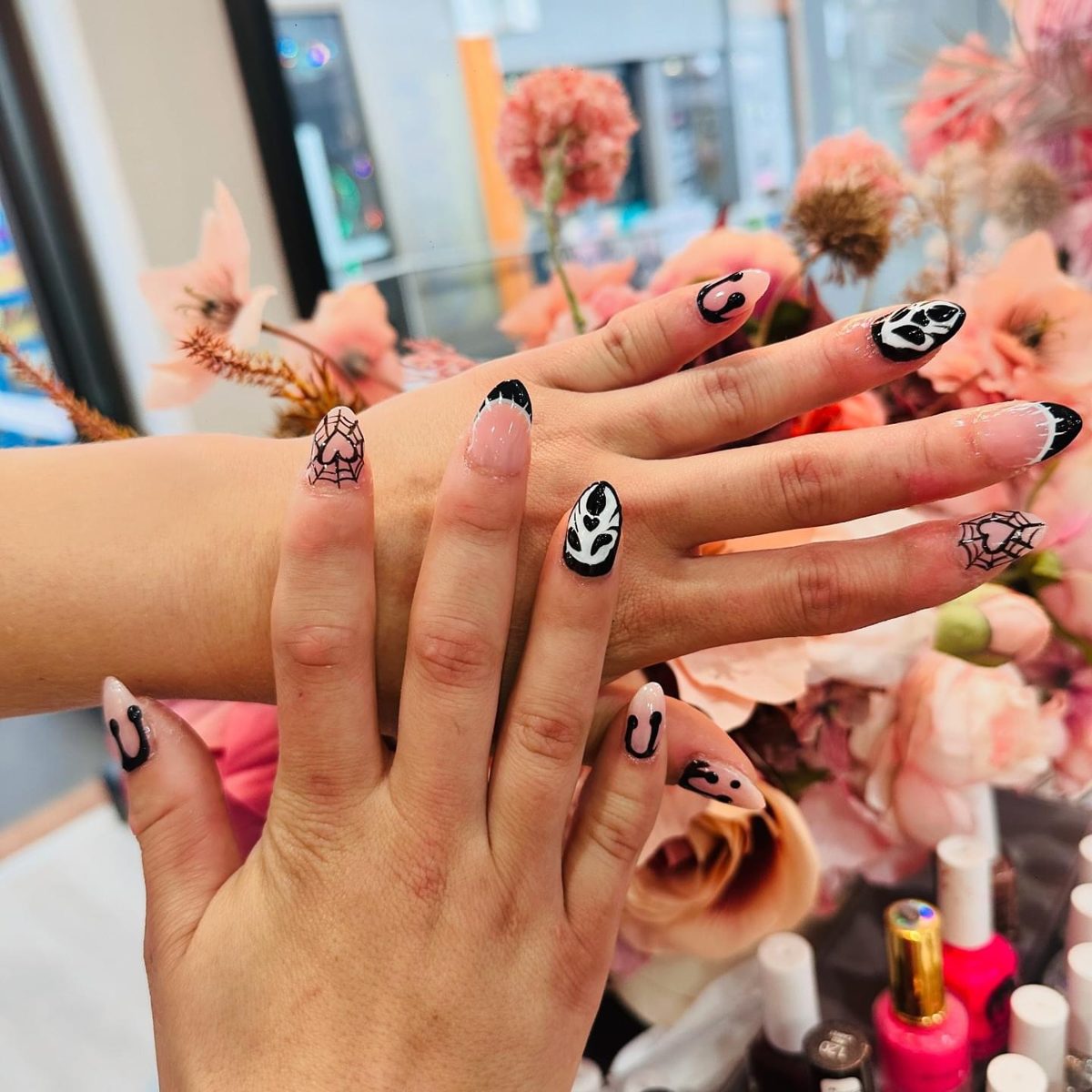 Black and white spiderweb nail art in front of the salon's flowers and polish shelf